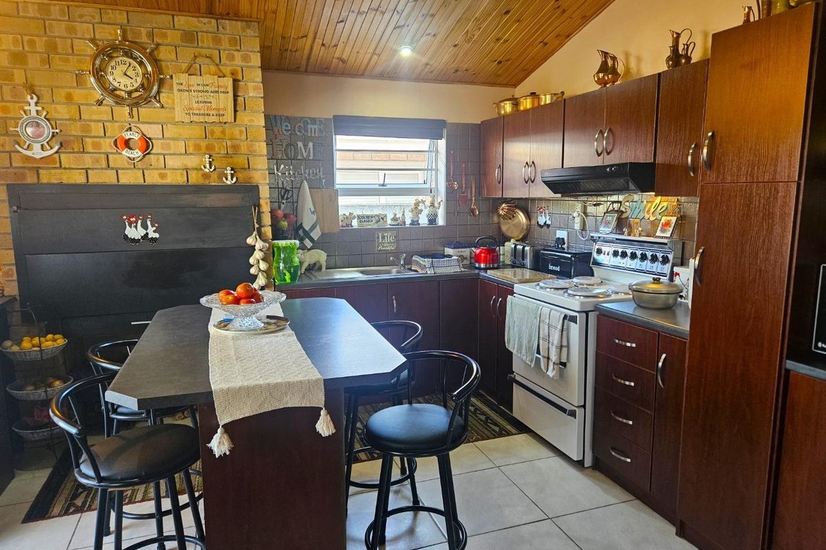A rustic-style kitchen featuring dark wood cabinetry, a brick feature wall, tiled flooring, and a timber-paneled vaulted ceiling with a central breakfast island.