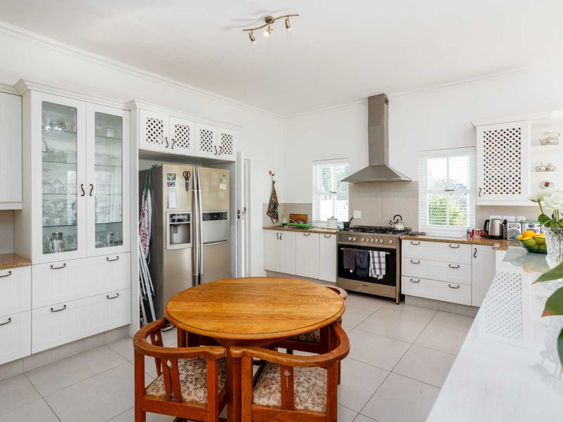 A bright, well-maintained kitchen featuring white cabinetry, stone countertops, stainless steel appliances, and tiled flooring, offering a clean and functional cooking space.