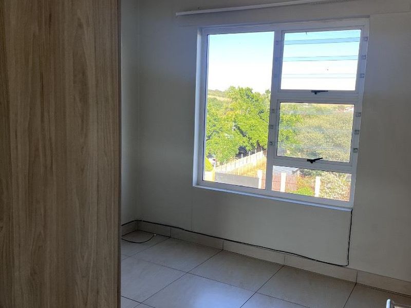 A bright, empty bedroom featuring neutral tiled flooring, a built-in cupboard, and a large window with views of the surrounding greenery.