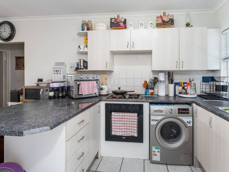 Compact kitchen featuring light-toned cabinetry, granite-look laminate countertops, built-in oven and hob, and an integrated washing machine.