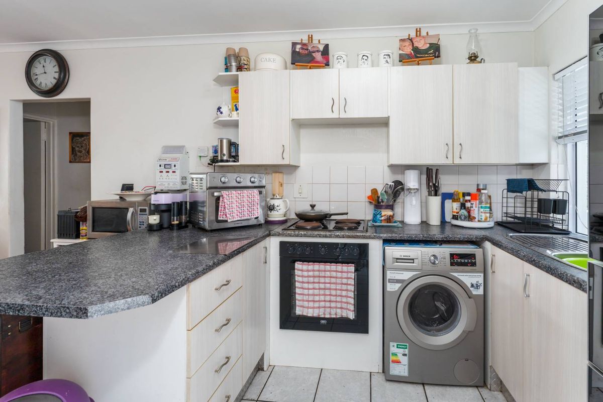 Compact kitchen featuring light-toned cabinetry, granite-look laminate countertops, built-in oven and hob, and an integrated washing machine.