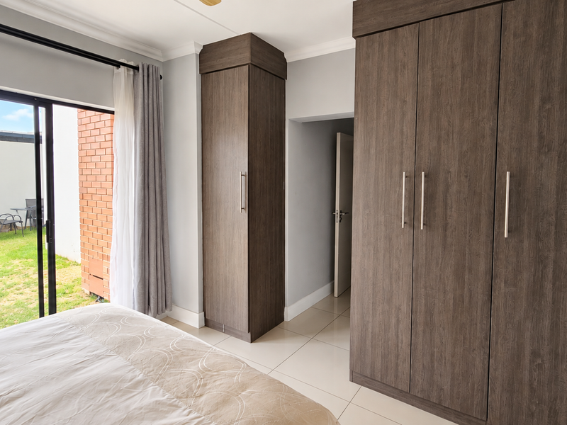 A well-maintained bedroom featuring modern dark wood built-in cupboards, tiled flooring, and a sliding glass door providing direct access to the garden.
