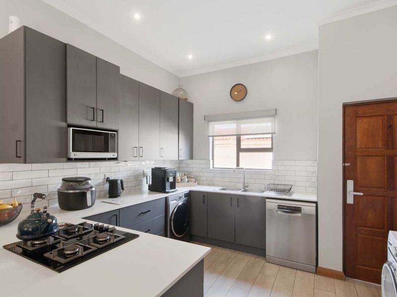 Modern kitchen featuring dark grey cabinetry, white countertops, subway tile backsplash, gas hob, and integrated appliances with wood-look laminate flooring.