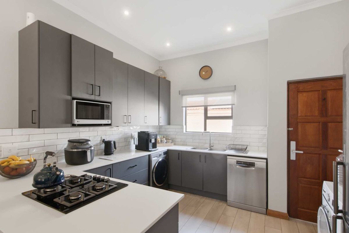 Modern kitchen featuring dark grey cabinetry, white countertops, subway tile backsplash, gas hob, and integrated appliances with wood-look laminate flooring.
