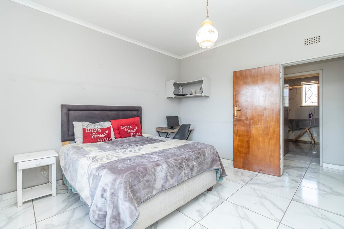 A bedroom featuring tiled flooring, coving, and a pendant light fixture, with an adjacent room visible through the timber door.