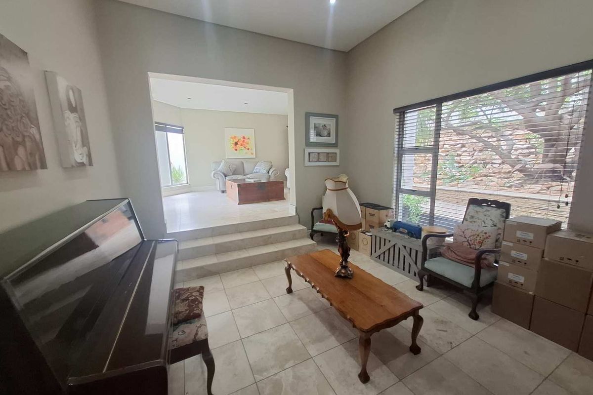 A split-level living area featuring tiled flooring, large windows with blinds, and a step-up transition to an adjacent lounge space.