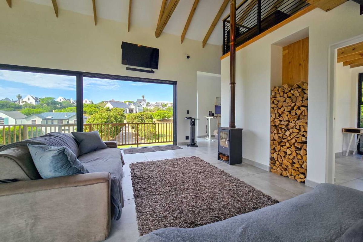 Spacious living area featuring a high vaulted ceiling with exposed timber beams, a modern wood-burning fireplace, and large sliding doors opening to a balcony.
