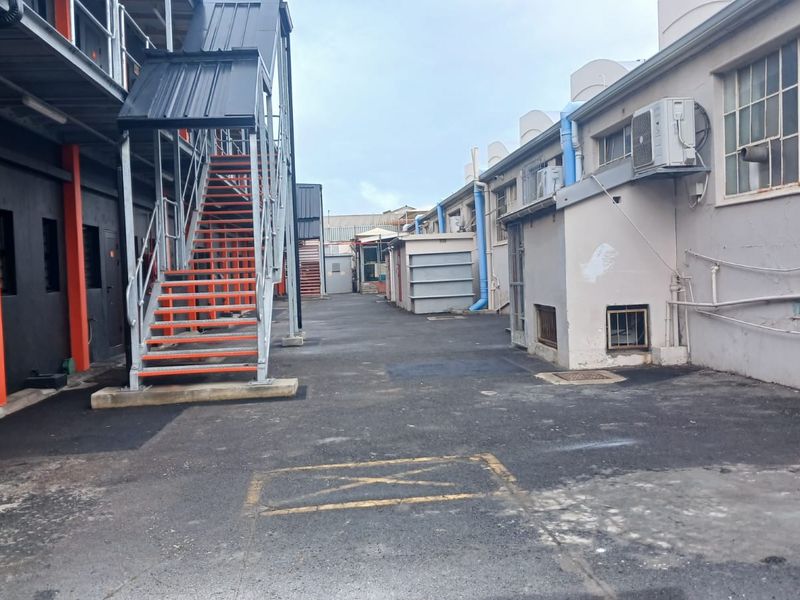 Rear industrial yard area featuring a metal staircase, asphalt paving, and exterior building access points with visible industrial infrastructure.