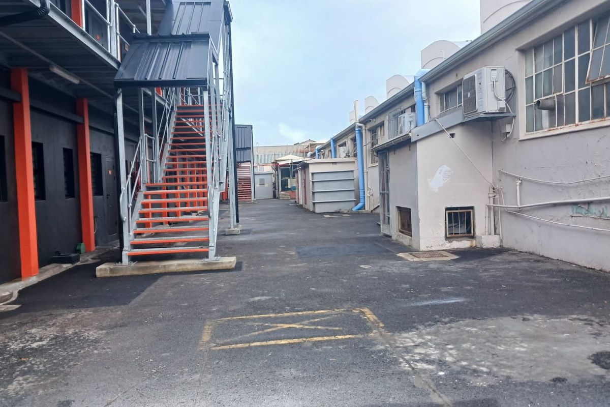Rear industrial yard area featuring a metal staircase, asphalt paving, and exterior building access points with visible industrial infrastructure.