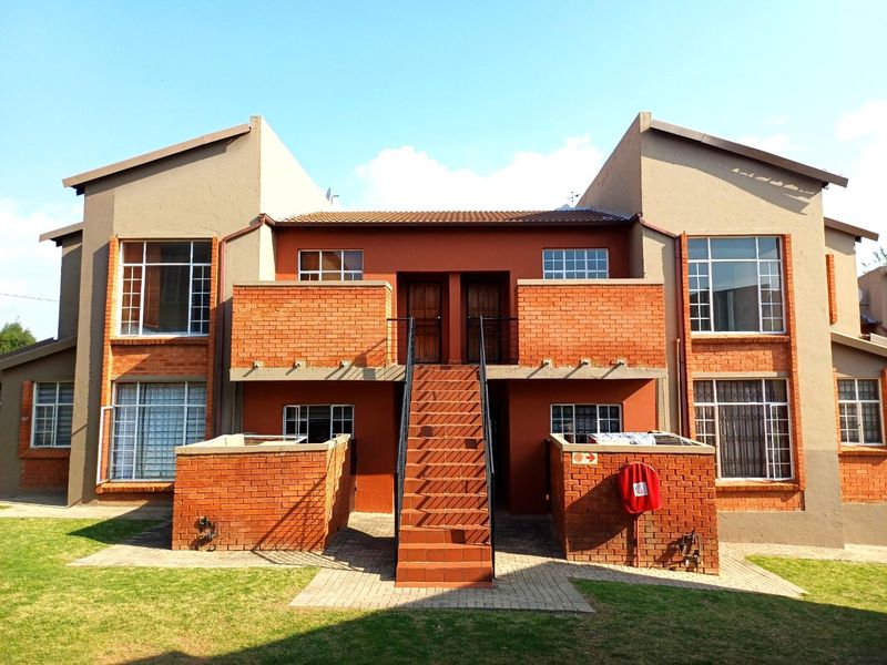 Front elevation of a two-story apartment complex featuring face-brick accents, external staircases, and well-maintained lawn areas.