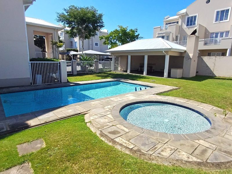 Outdoor pool area featuring a swimming pool, circular spa, stone paving, and a covered patio with an outdoor fireplace.