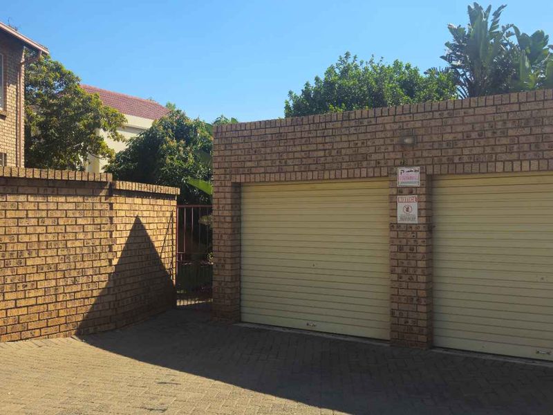 A double garage with face brick exterior and paved driveway access, situated within a townhouse complex.
