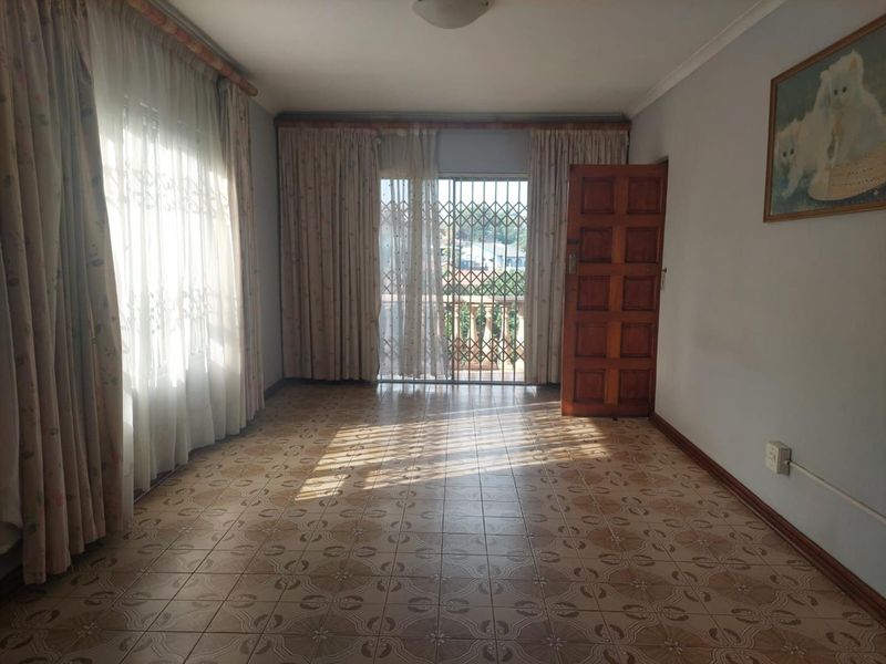 A spacious, empty living room featuring tiled flooring, a timber door, and a security gate leading to an outdoor area.
