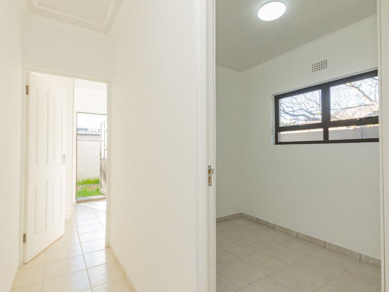 A clean, empty hallway with tiled flooring leading to an adjacent room and an exterior doorway.