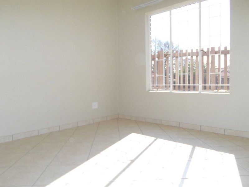 A bright, empty bedroom featuring neutral tiled flooring and a large window with security bars, offering a clean canvas for personalization.