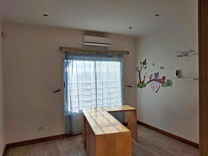 A bedroom featuring laminate flooring, recessed downlights, and a wall-mounted air conditioning unit. The space is currently vacant and ready for personalization.