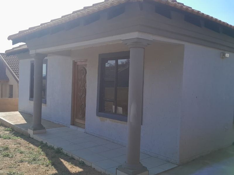 Front exterior view of a single-story house featuring a covered tiled porch with decorative columns and a timber entrance door.