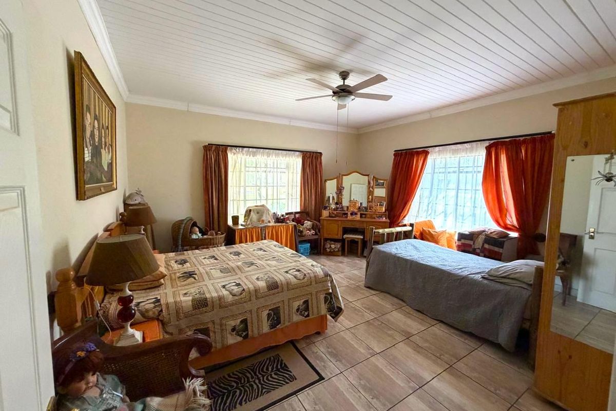Spacious bedroom featuring tiled flooring, a ceiling fan, and timber-look ceiling panels, offering a functional layout with security bars on the windows.