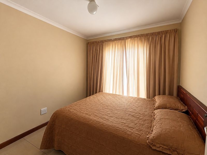 A neutrally painted bedroom featuring tiled flooring, cove cornicing, and natural light filtered through full-length curtains.
