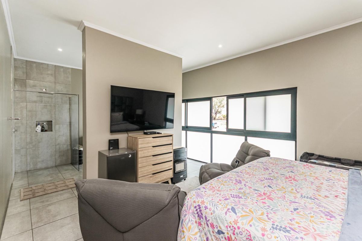 A spacious bedroom featuring an open-plan layout with an integrated en-suite bathroom, large sliding windows, and neutral wall finishes.