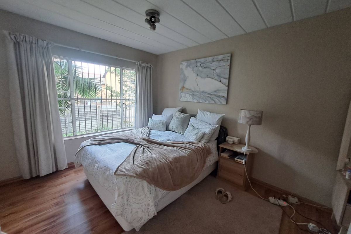A cozy bedroom featuring wood-look flooring, a large window with security bars, and a neutral color palette.