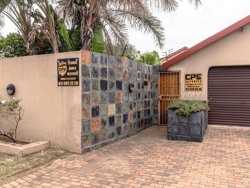 Front exterior view featuring a brick driveway, slate-tiled boundary wall, security gate, and a roller garage door with integrated security signage.