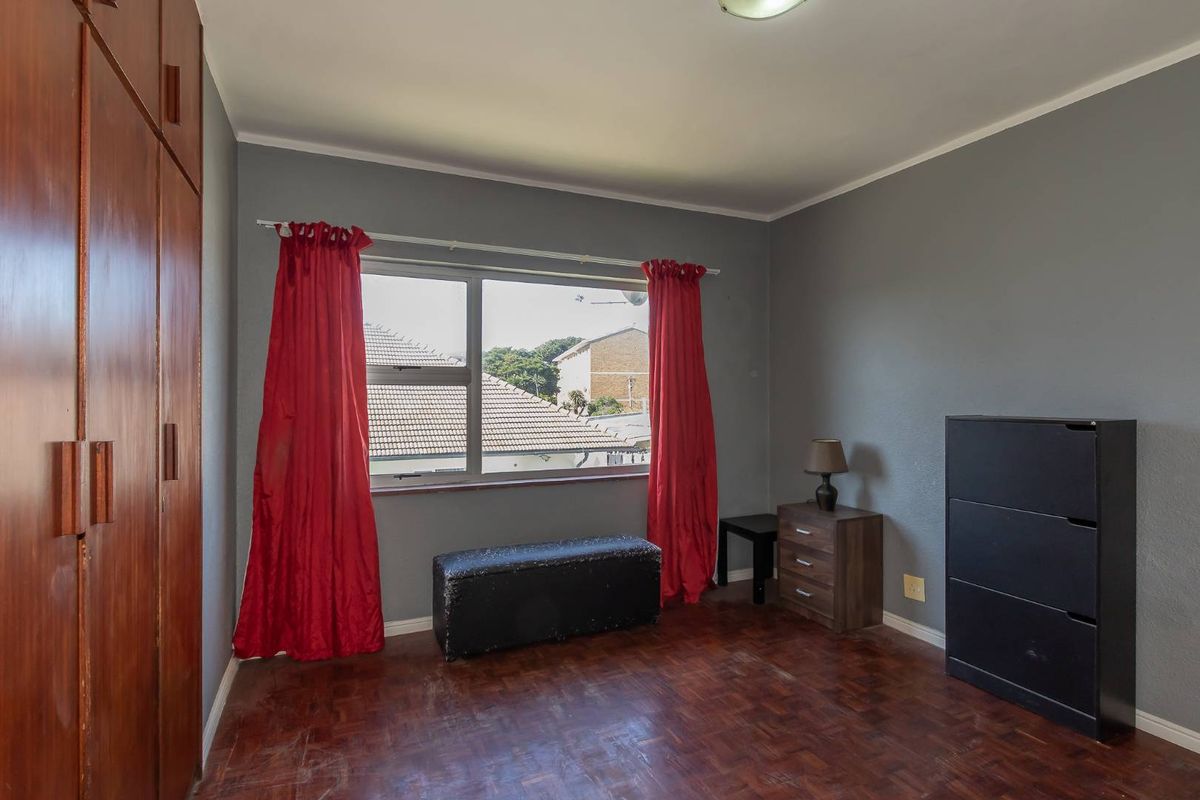 A bedroom featuring parquet flooring, built-in wooden cupboards, and an aluminium window frame, offering a functional space with potential for cosmetic updates.