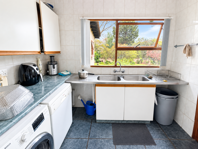 Functional laundry area featuring a double stainless steel sink, tiled splashbacks, and built-in cabinetry with space for under-counter appliances.