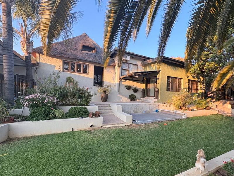 Rear view of a house featuring a thatched roof, paved patio area, and tiered landscaped garden with retaining walls.