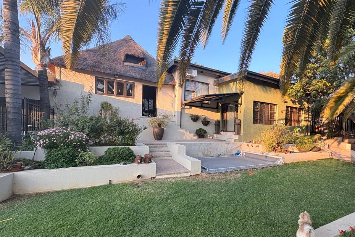 Rear view of a house featuring a thatched roof, paved patio area, and tiered landscaped garden with retaining walls.