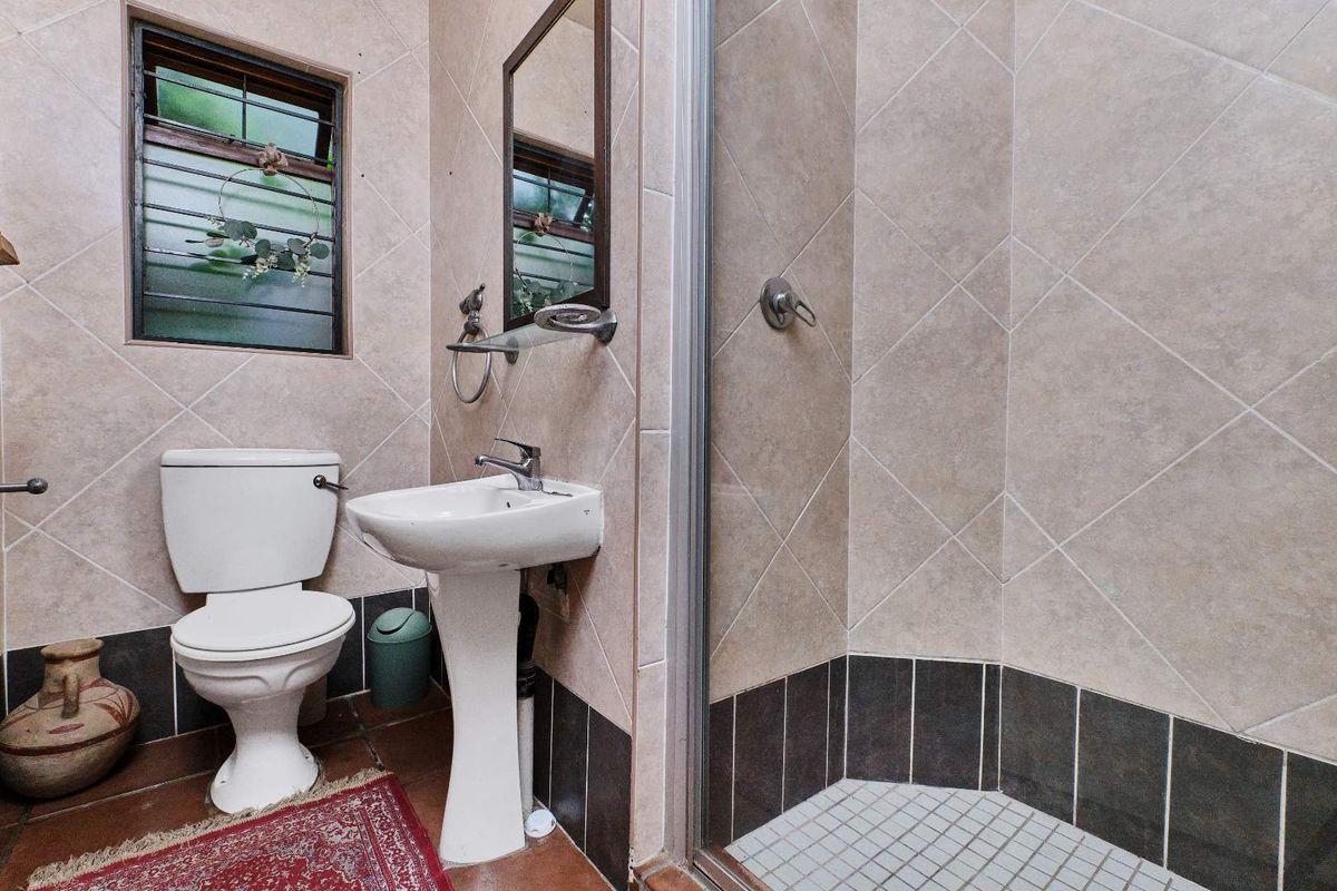 A compact bathroom featuring a pedestal basin, toilet, and a corner shower enclosure with tiled walls and flooring.