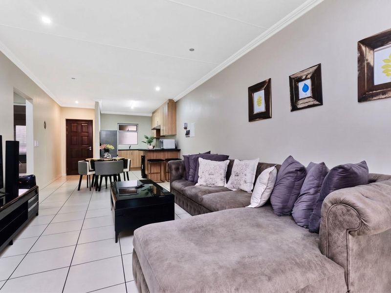 Spacious open-plan living area featuring tiled floors, recessed lighting, and a functional kitchen with a breakfast counter, creating a seamless flow throughout the apartment.