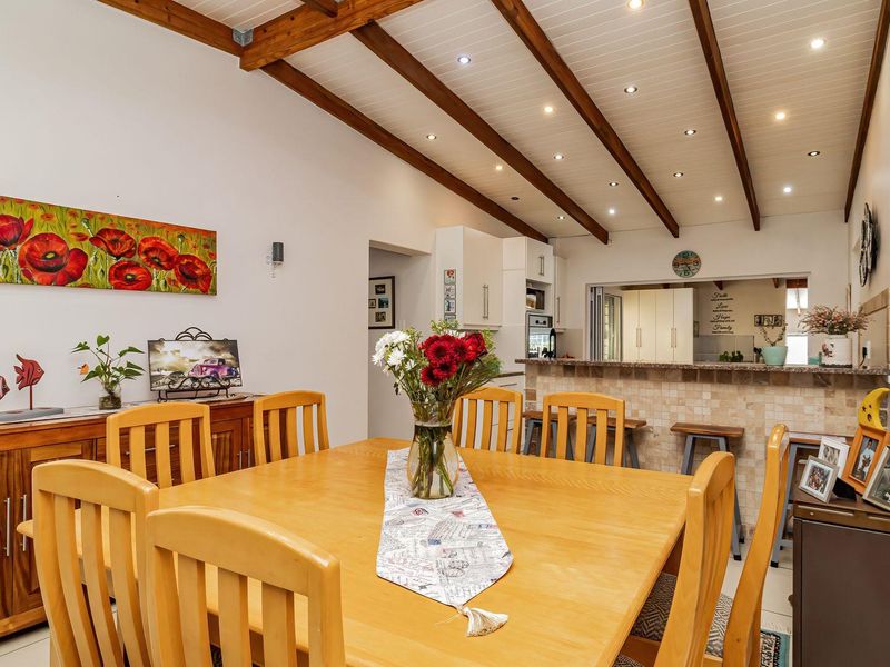 Open-plan dining and kitchen area featuring exposed timber ceiling beams, recessed lighting, and a stone-clad breakfast bar connecting the two spaces.