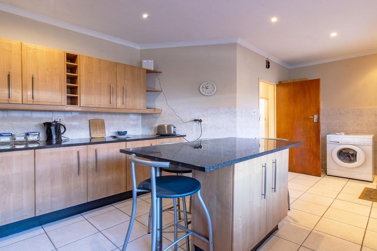Functional kitchen featuring light wood cabinetry, granite countertops, a central island, and tiled flooring with integrated laundry plumbing.