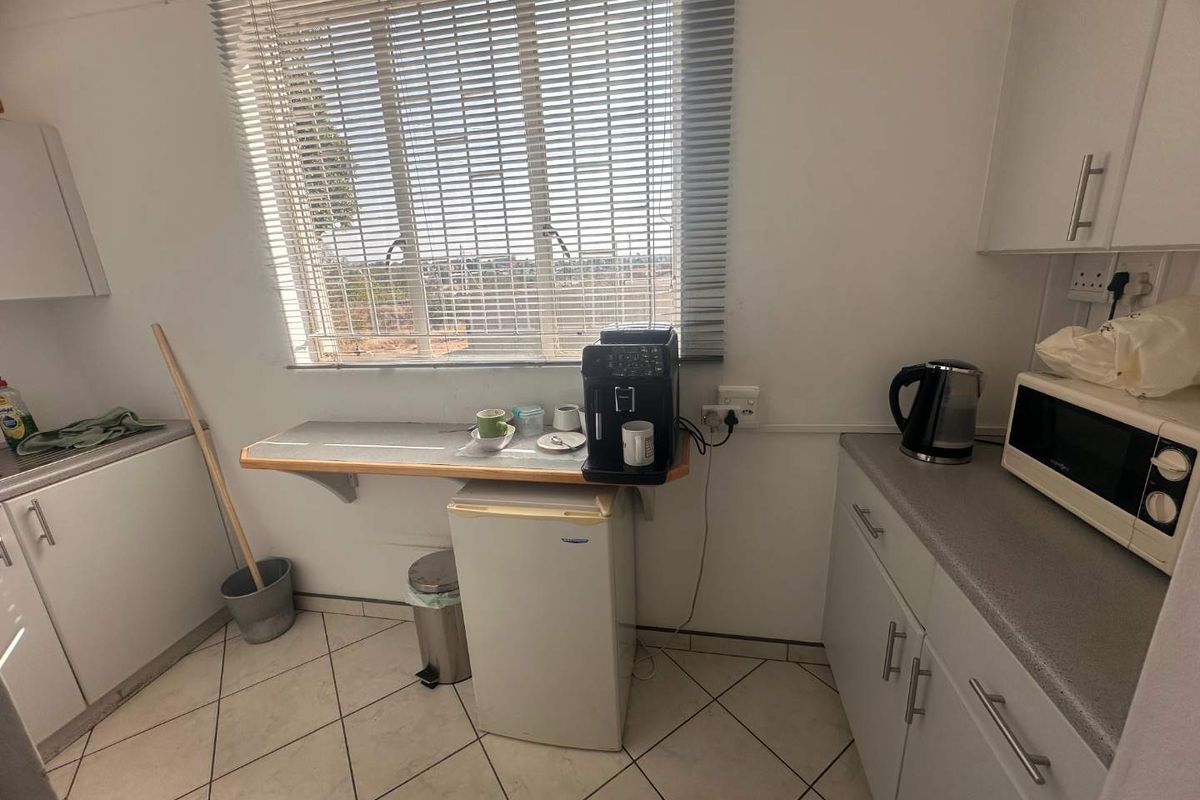 A functional kitchen area featuring tiled flooring, built-in cabinetry, laminate countertops, and a window with venetian blinds.