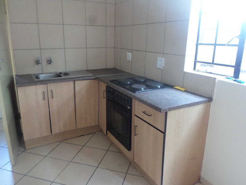 A compact kitchen featuring laminate cabinetry, a built-in oven with electric hob, stainless steel sink, and neutral ceramic wall and floor tiling.