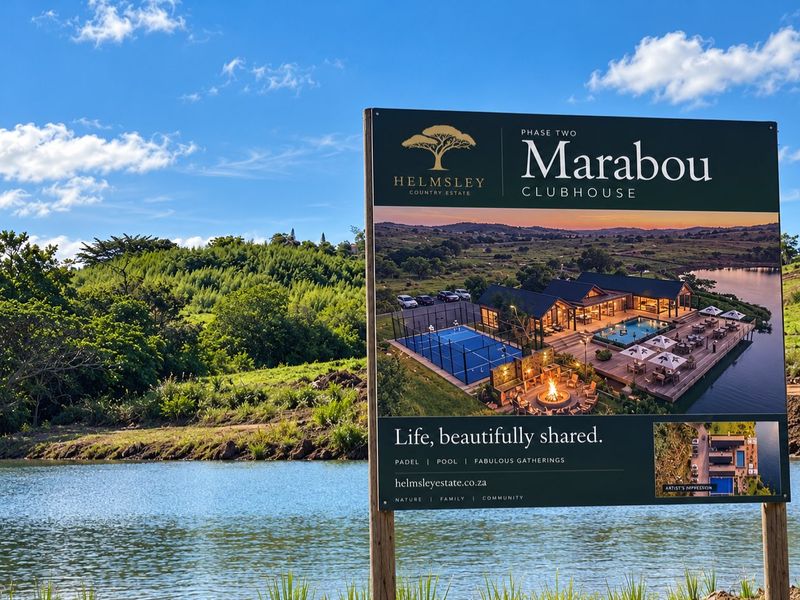 A large promotional billboard showcasing the Marabou Clubhouse development, situated on a scenic vacant land plot overlooking a lake.