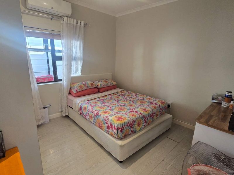 A functional bedroom featuring laminate flooring, a wall-mounted split-system air conditioner, and a window with natural light.