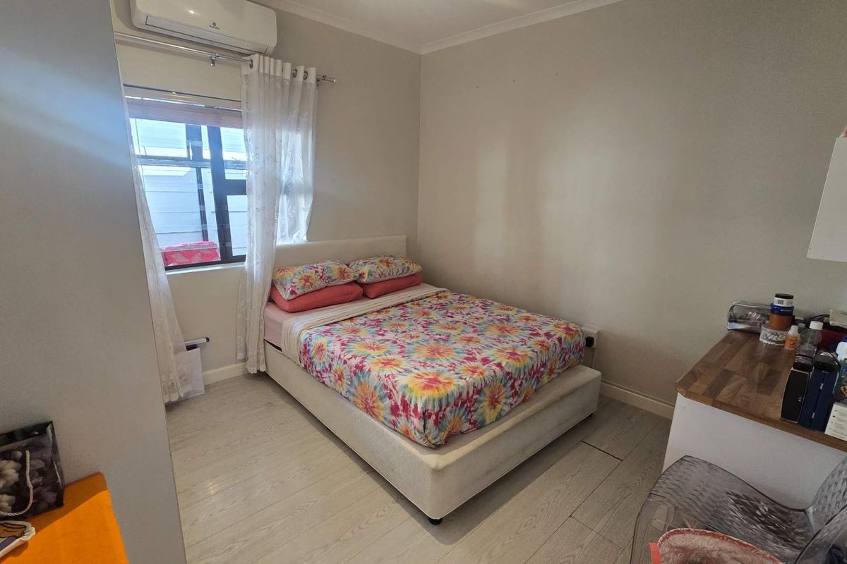 A functional bedroom featuring laminate flooring, a wall-mounted split-system air conditioner, and a window with natural light.