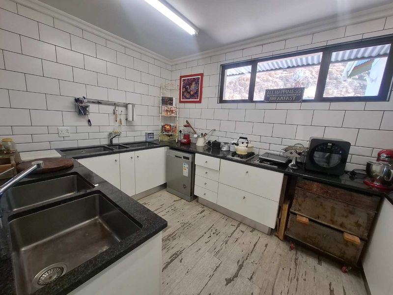 Functional kitchen featuring white cabinetry, granite countertops, subway tile backsplash, and double stainless steel sinks with ample workspace.