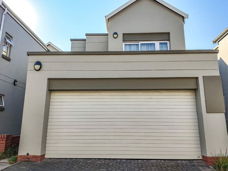 Front elevation of a modern cluster home featuring a double garage door, paved driveway, and neutral exterior finishes.