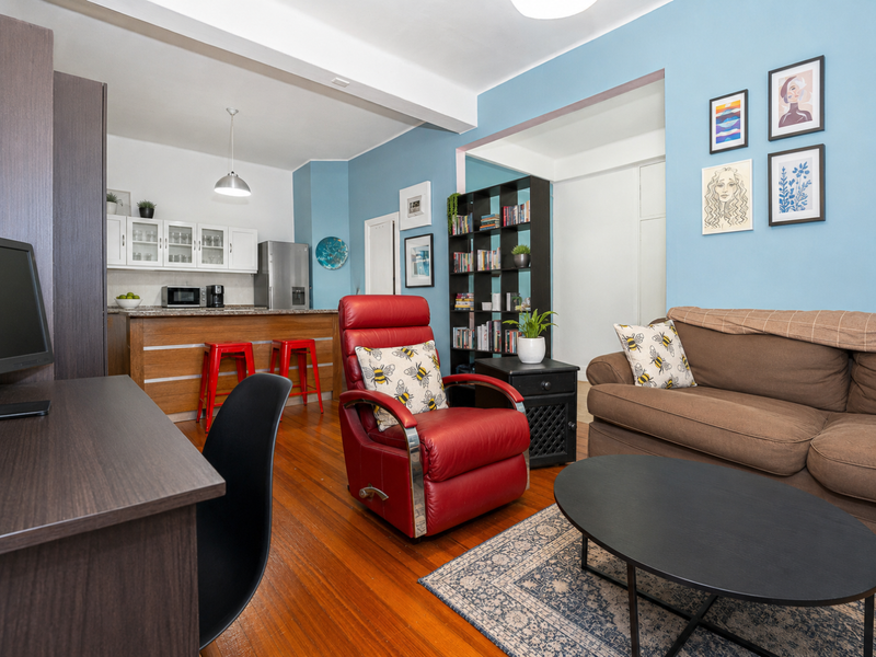 Open-plan living area featuring hardwood flooring and a functional kitchen with stone countertops and cabinetry, creating a versatile and connected living space.