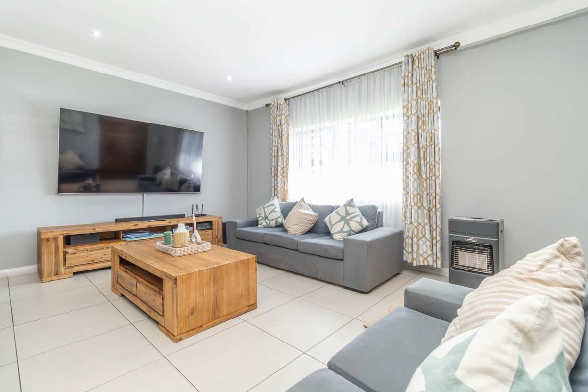 A bright and well-maintained living room featuring neutral tiled flooring, recessed ceiling lighting, and large windows with curtain tracks.