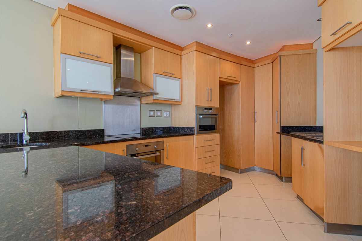 A functional kitchen featuring light wood cabinetry, dark granite countertops, integrated oven, and stainless steel extractor fan with tiled flooring.