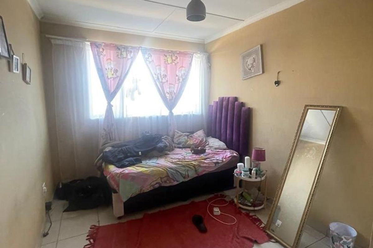 A bedroom featuring tiled flooring and a central pendant light fitting, requiring cosmetic updates to the walls and ceiling.