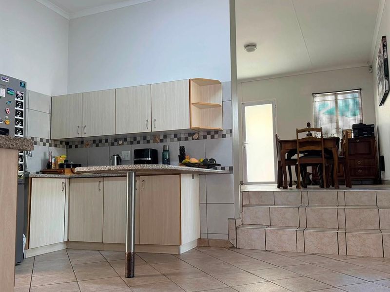 Open plan kitchen area featuring built-in cabinetry, granite countertops, and tiled flooring, with a raised dining area accessible by tiled stairs.