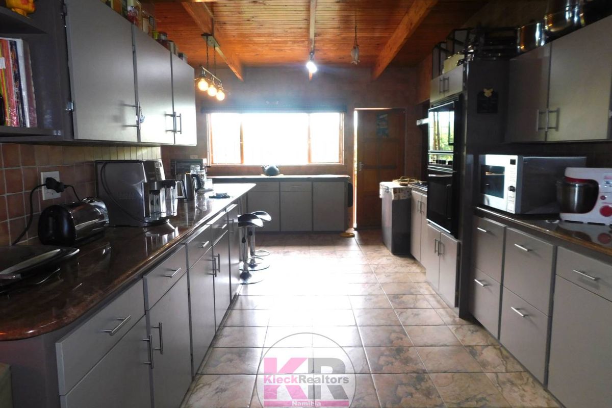 Spacious kitchen featuring extensive grey cabinetry, granite countertops, tiled flooring, and a rustic exposed timber beam ceiling with integrated lighting.