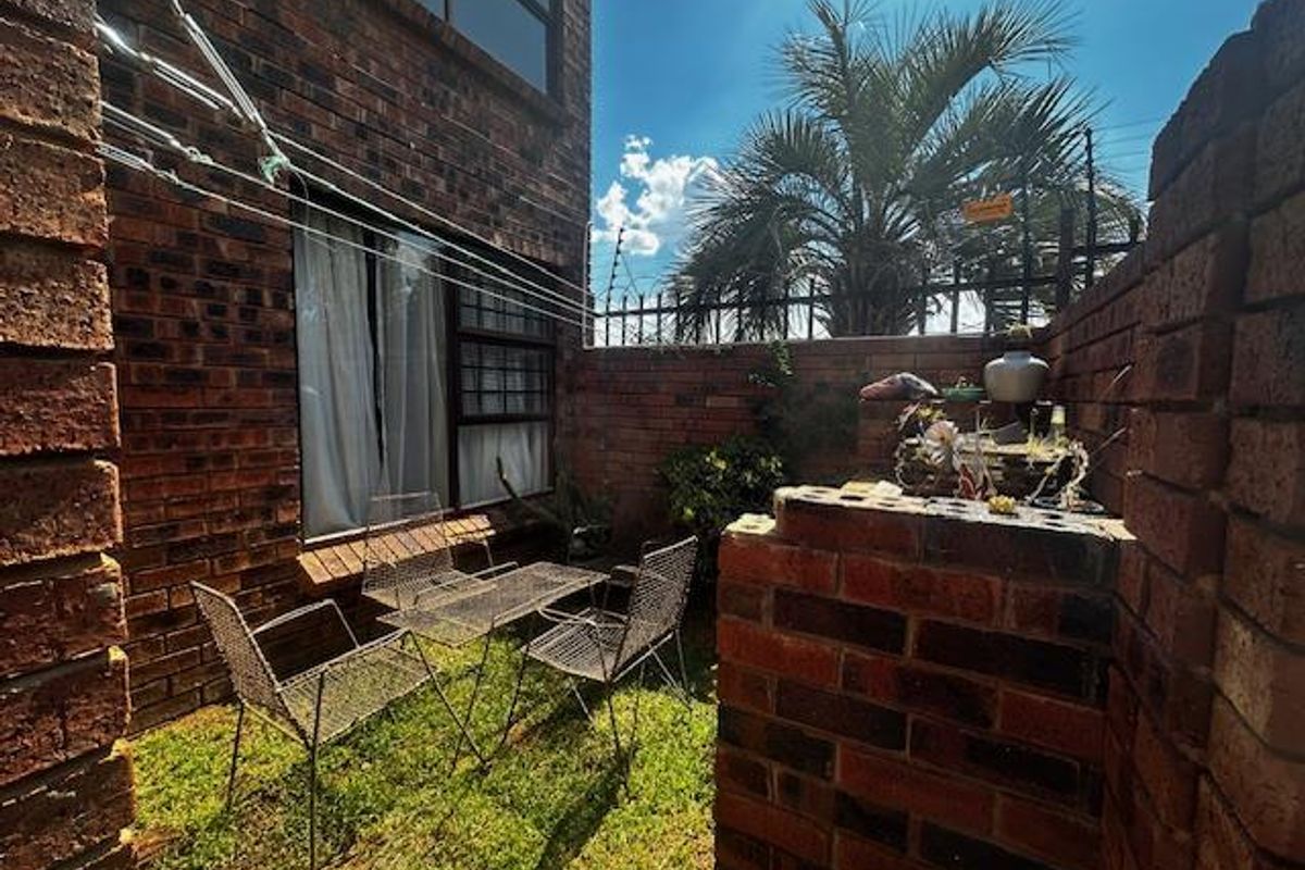 A private rear courtyard featuring exposed brick walls, a small lawn area, and direct access to the townhouse interior.