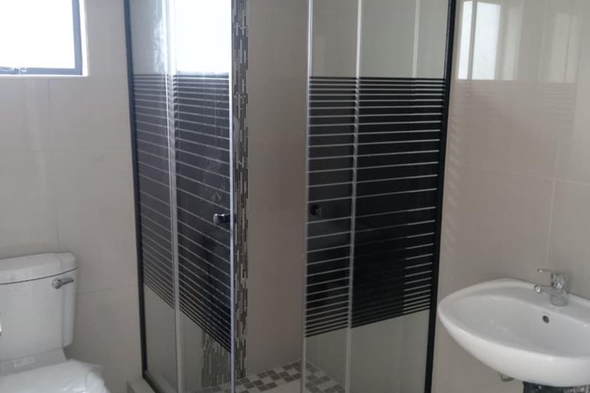 A modern bathroom featuring a corner shower enclosure with black framing, a wall-mounted basin, and a standard toilet.
