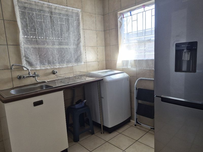 A functional laundry area featuring tiled walls and flooring, a stainless steel sink, and dedicated space for laundry appliances.